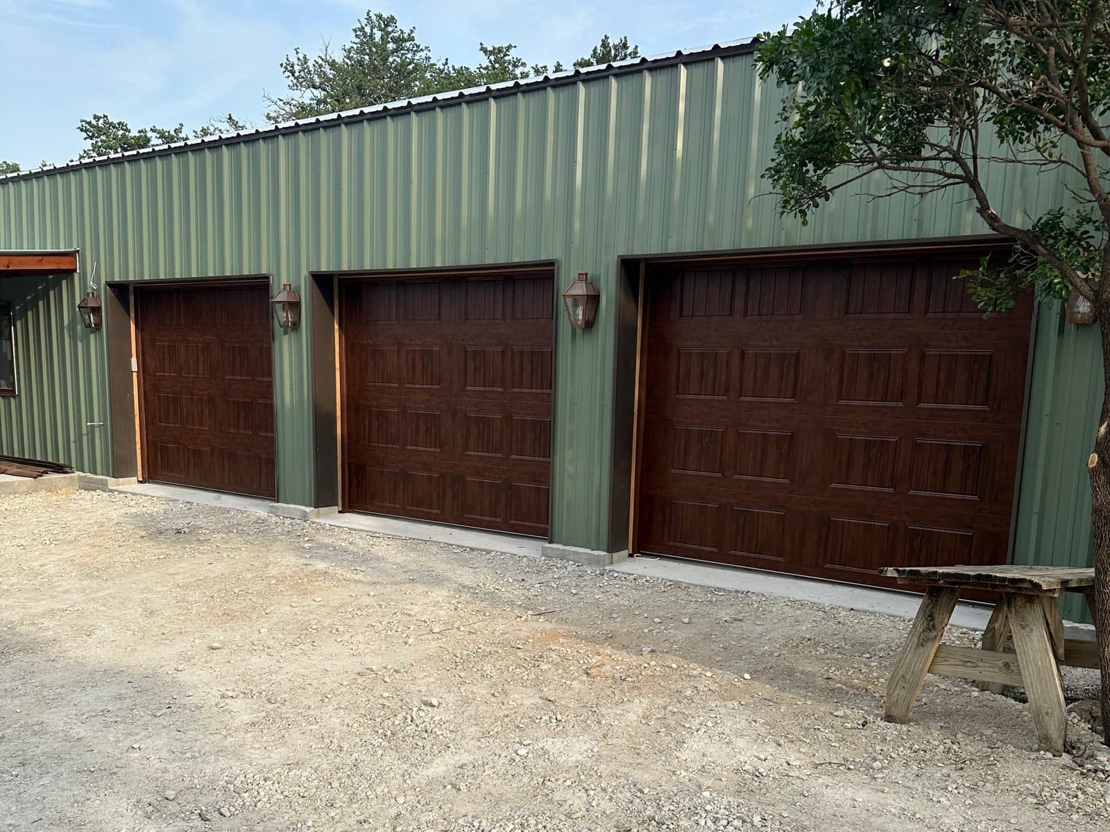 Three matching walnut garage doors on a sage green building with copper lanterns